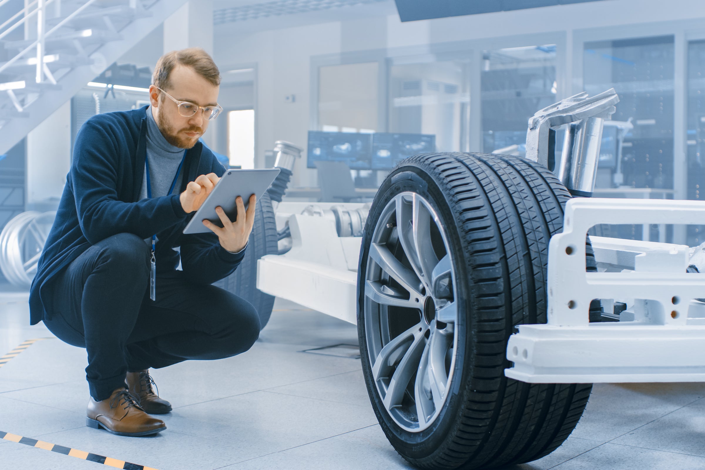 Engineer in an automotive laboratory works on a tablet and evaluates a car prototype