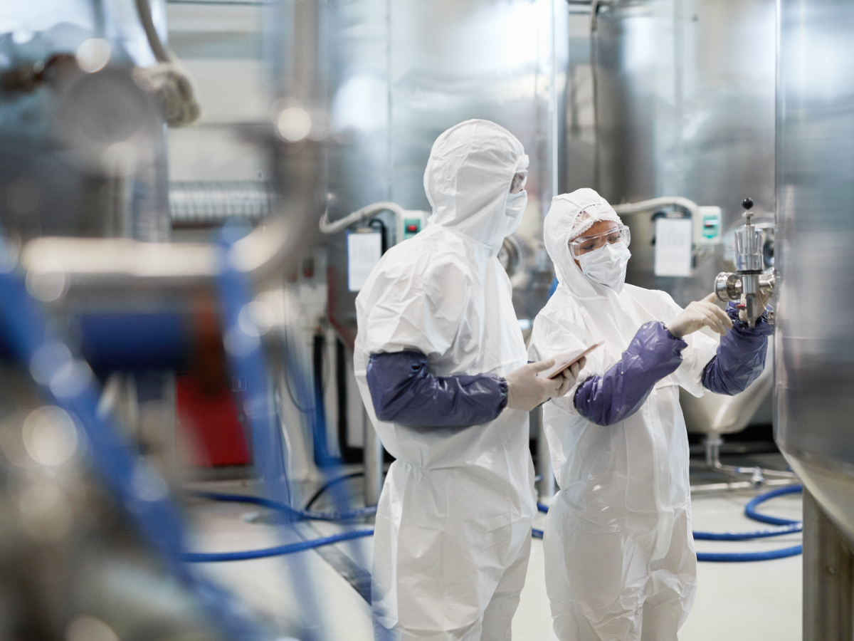 Two workers in full PPE checking pressure on a large tank