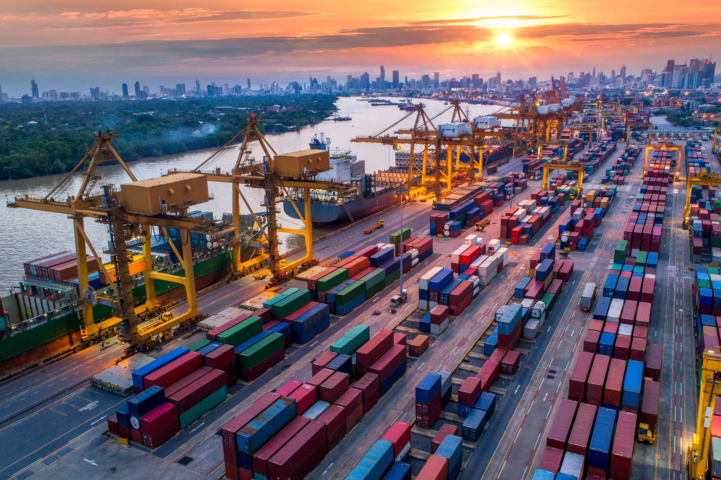 Container cargo ship and cargo plane with working crane bridge in shipyard at sunrise