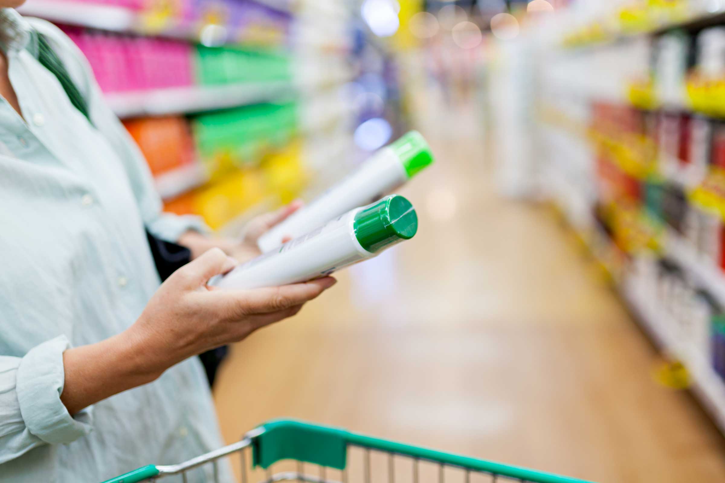 Person comparing green and white plastic bottles in a supermarket