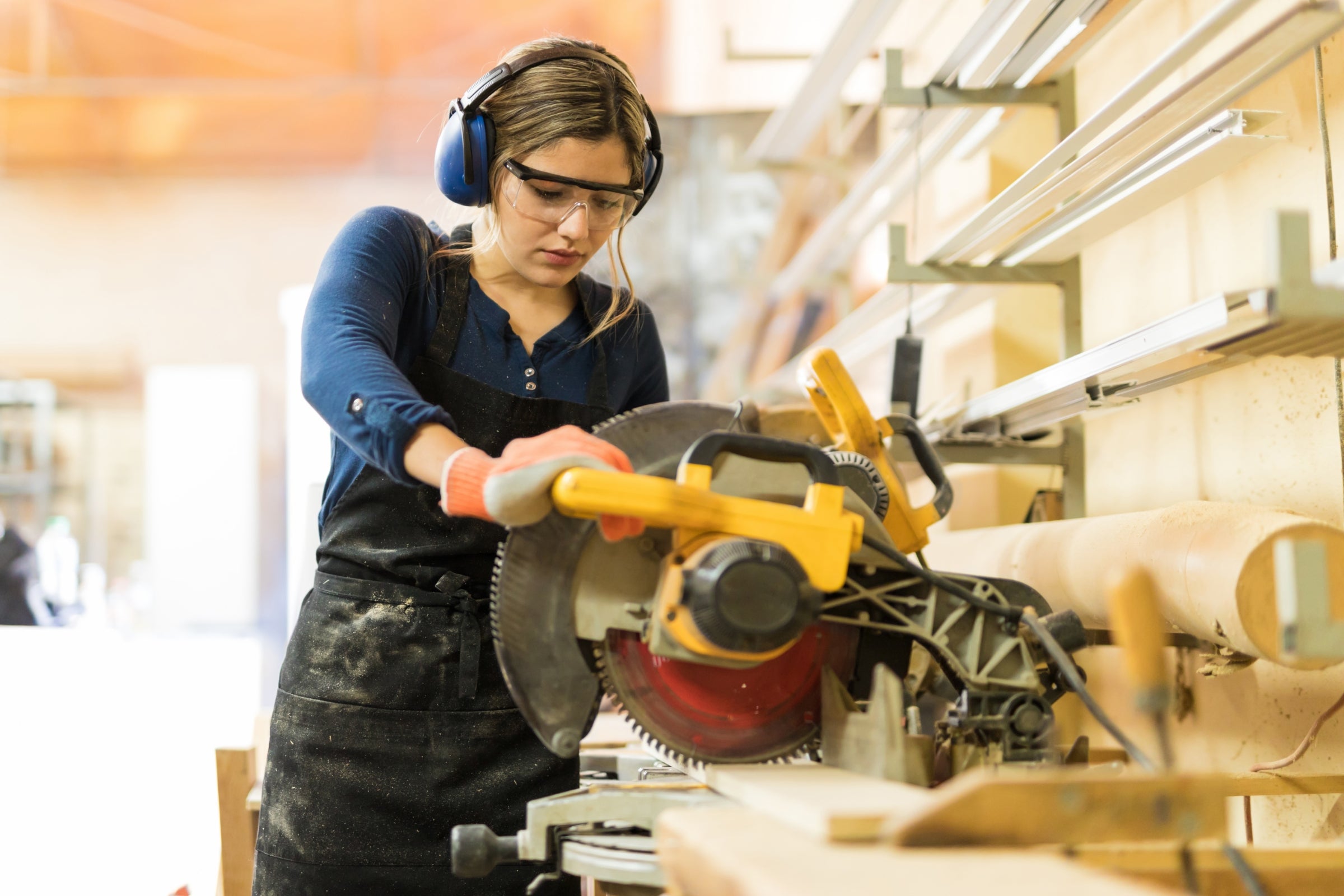 A female carpenter using a circular saw in a woodshop.