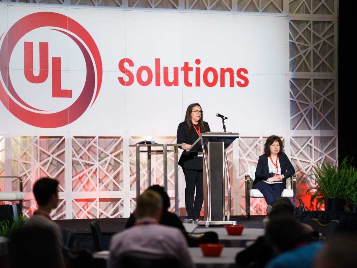 Two speakers giving a presentation on a stage. The UL Solutions logo is behind them