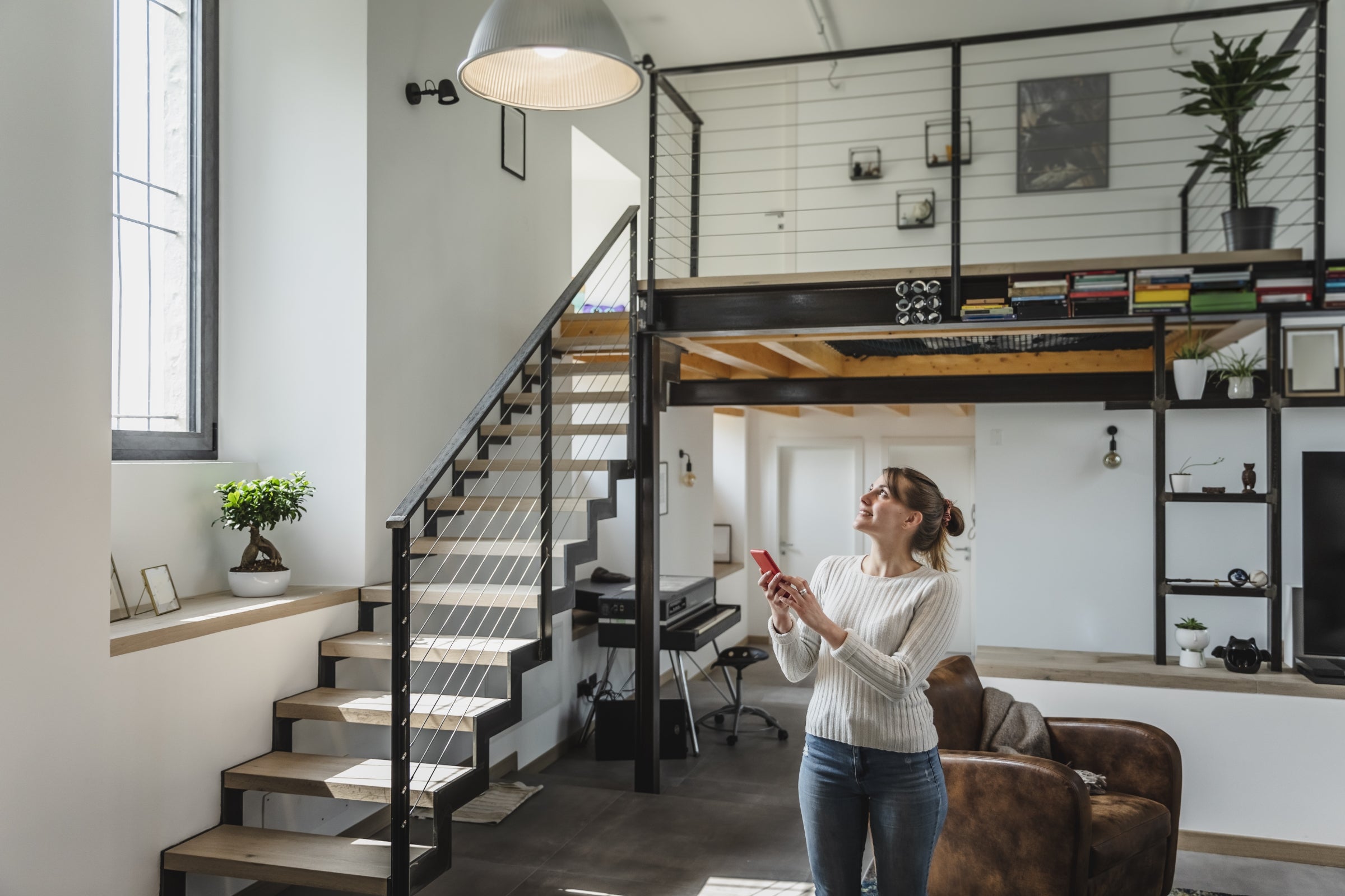 Young woman controlling smart home functions through mobile phone at modern home.