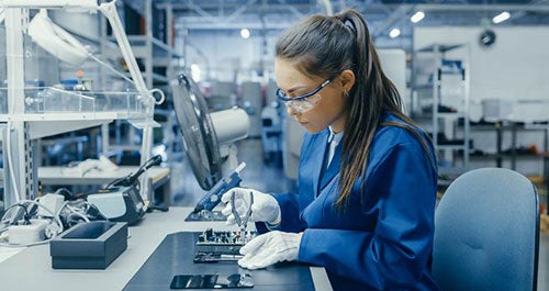 a person wearing protective gloves and safety glasses, working with a computer board