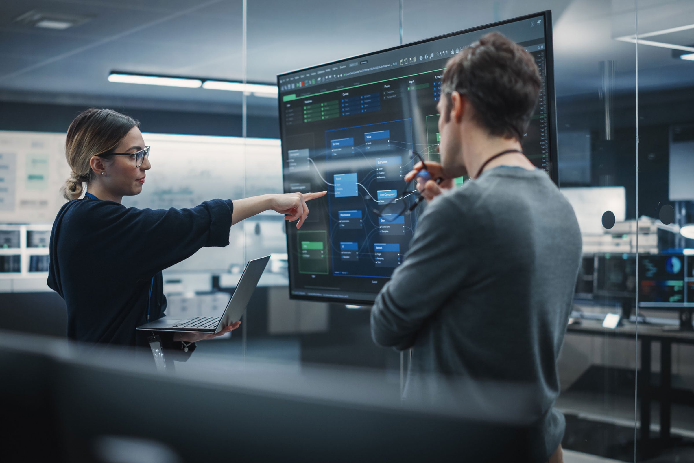 a person pointing at a screen, with another person watching