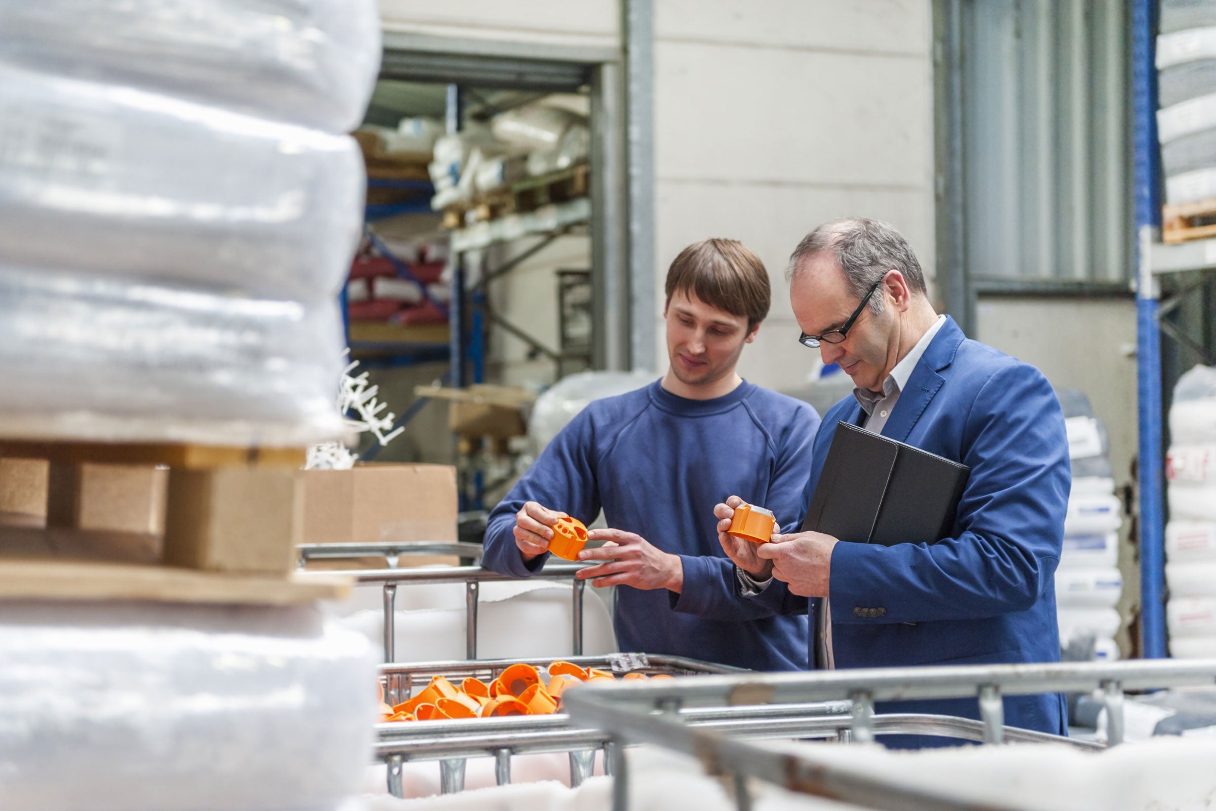 Two people inspecting a batch of orange plastic parts inside a warehouse