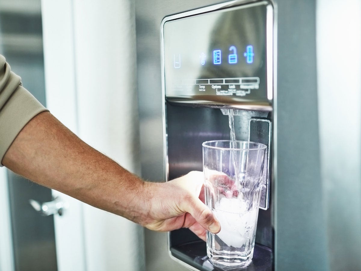 Closeup of a person filling a glass with water from the dispenser on a refrigerator 