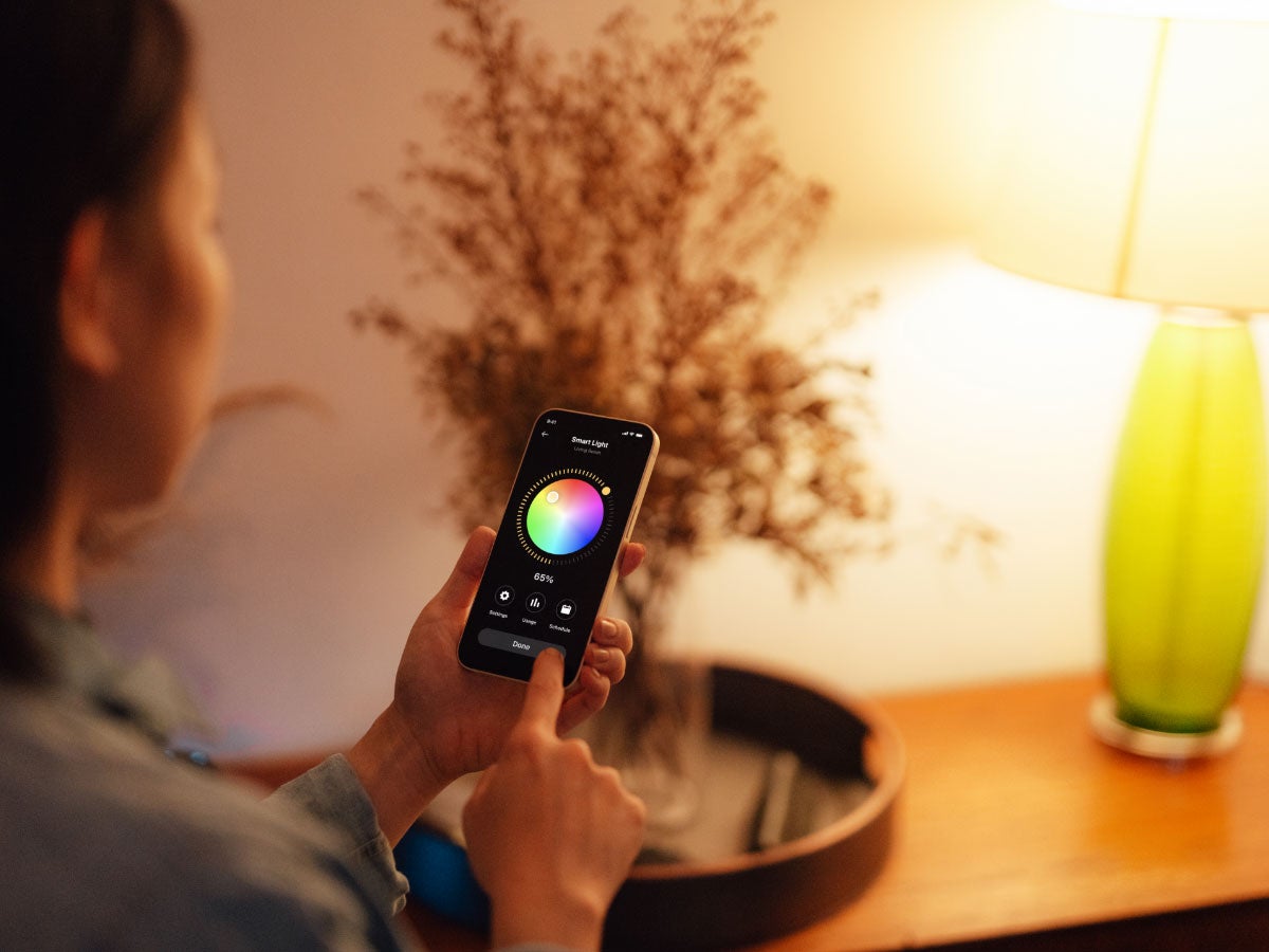 Person using an app to control the color of the light coming from a nearby desk lamp