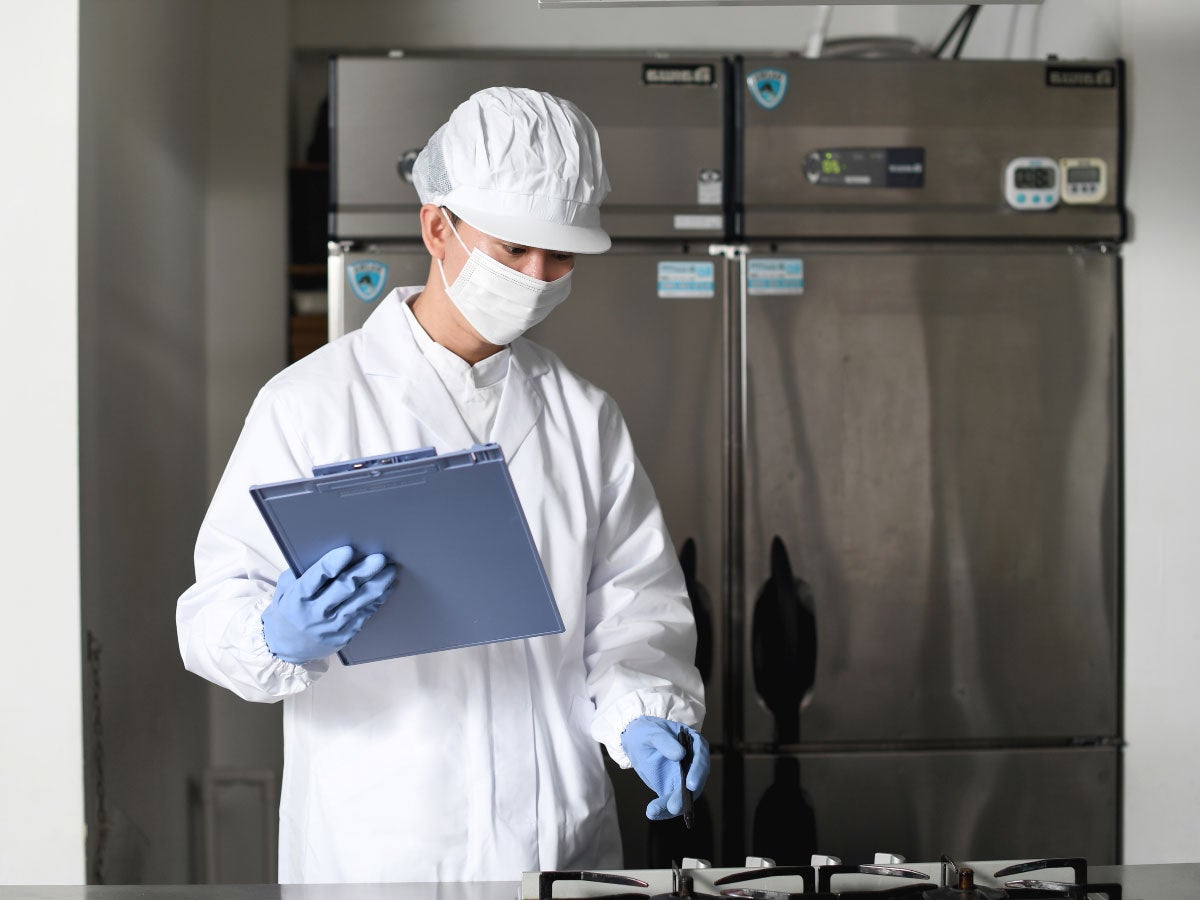 Inspector holding a clipboard while inspecting kitchen equipment