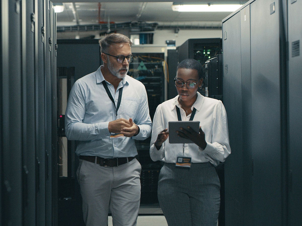 Two IT technicians reviewing information on a tablet inside a inside a server room