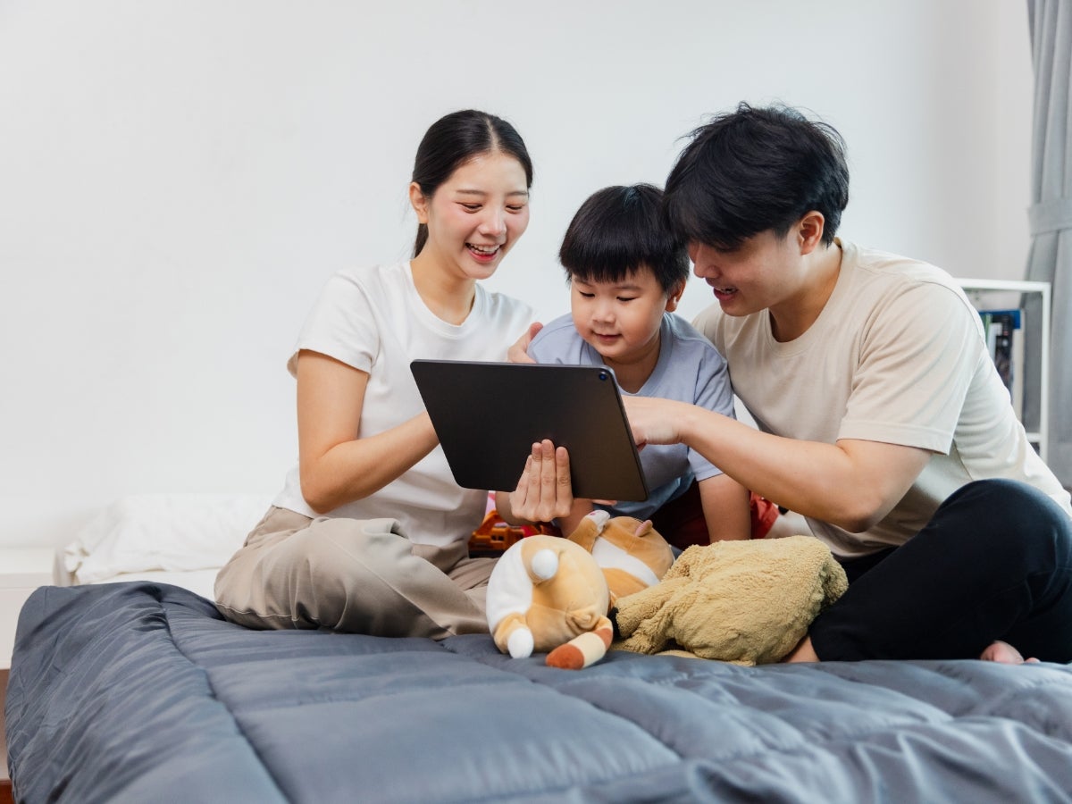 Family spending quality time together on a bed while enjoying an educational activity on a tablet.