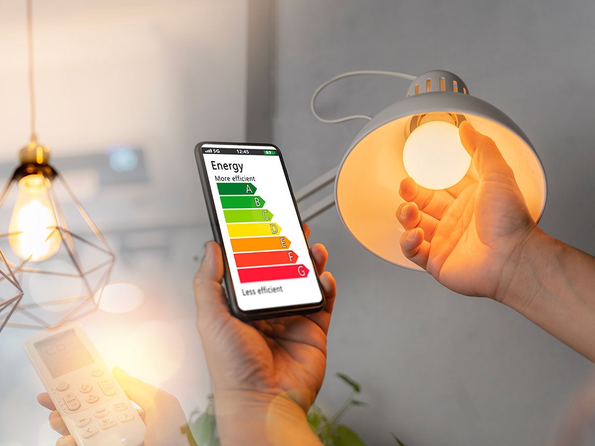 Person adjusting a lightbulb while looking at energy efficiency readings on a mobile device