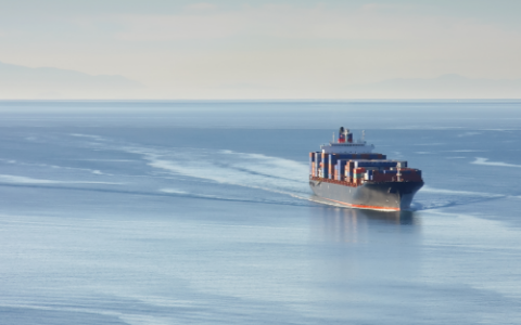 Distant aerial photo of a loaded container ship at sea.