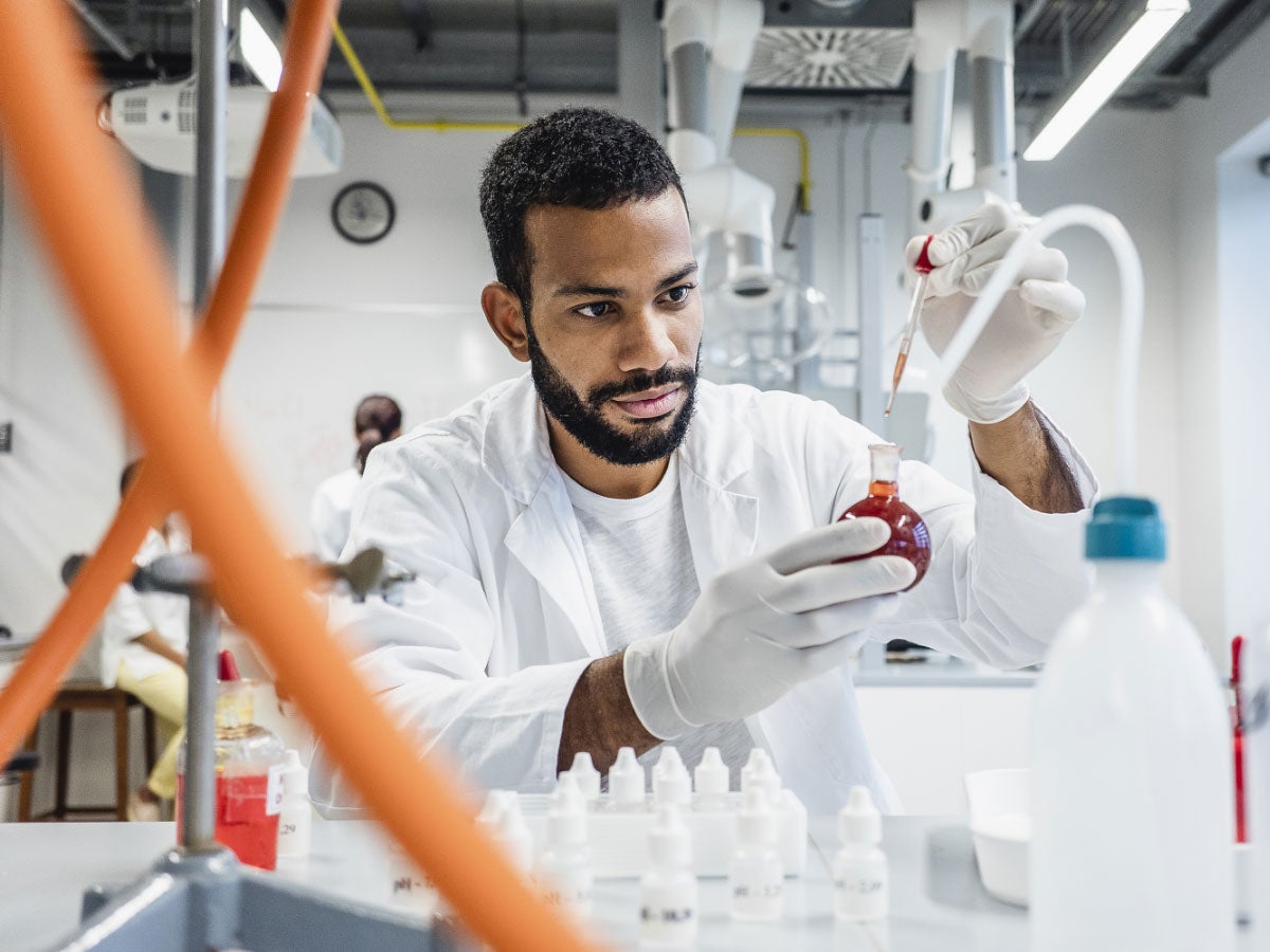 A person in a laboratory inspecting a liquid in a flask