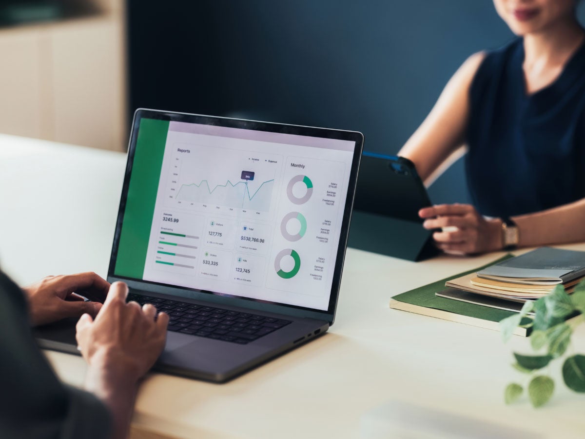 Two people on laptops, one monitor showing software with charts