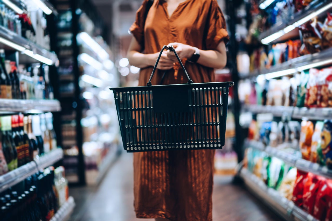 woman holding basket in center of aisle at grocery store
