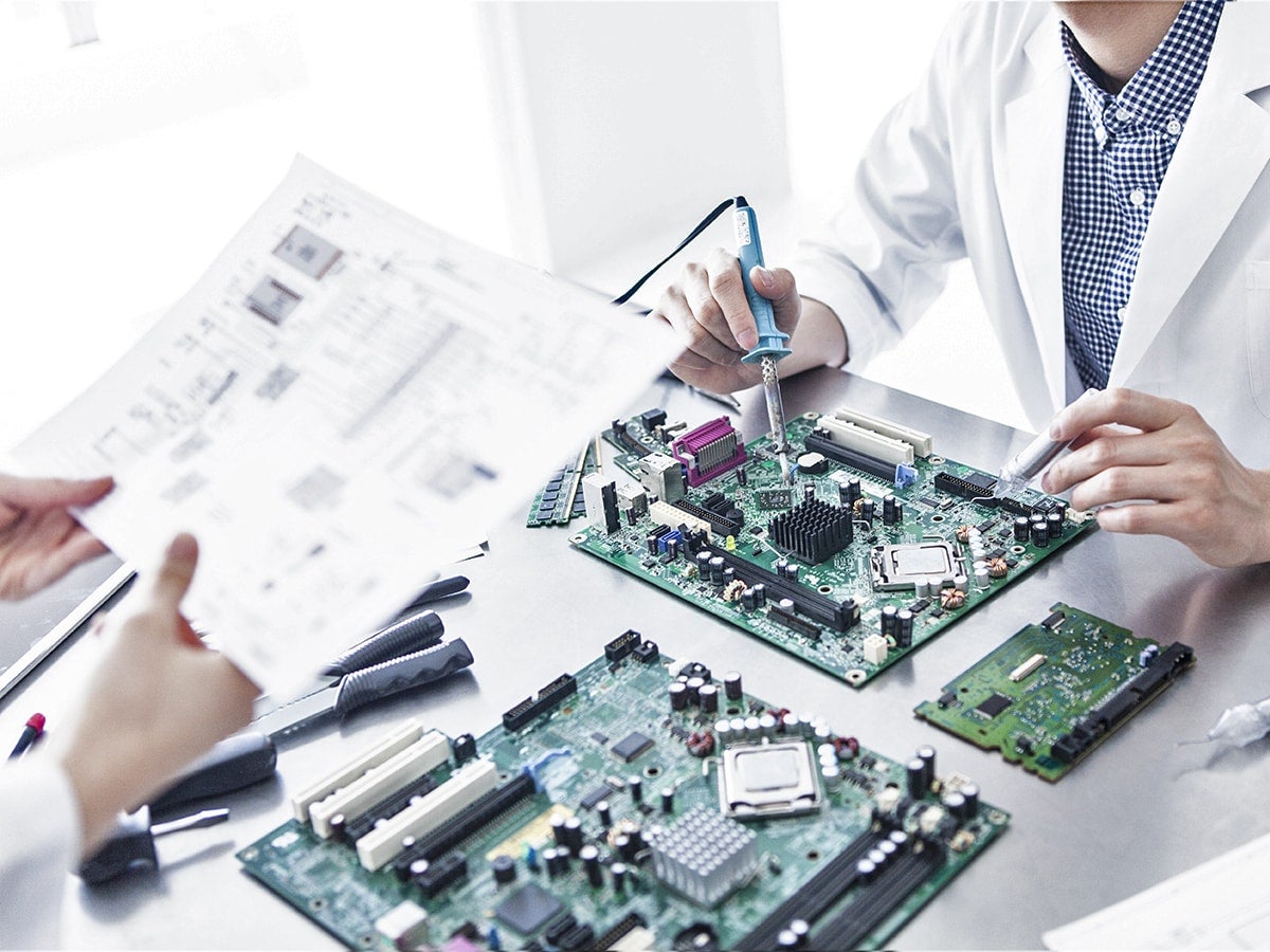 Lab workers in white coats soldering and reviewing circuit boards.