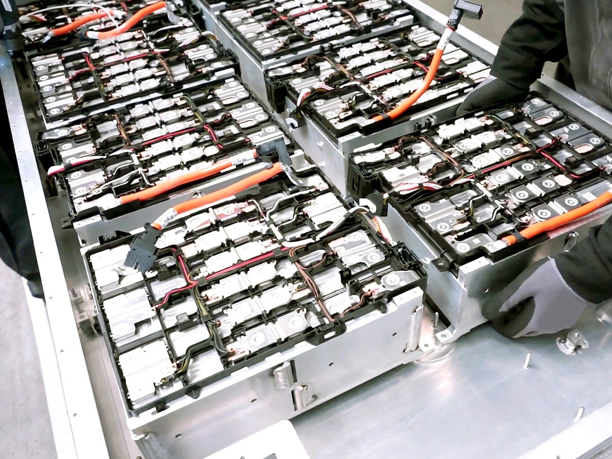 Gloved workers assembling an electric vehicle battery pack with orange high‑voltage cables.