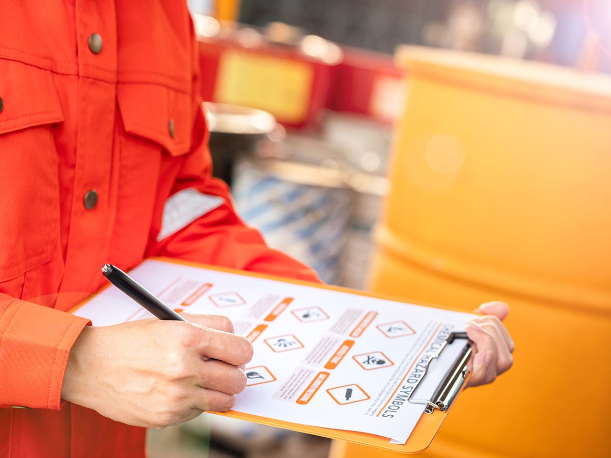 A person inspecting a chemical container and writing a report