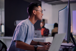 A person working on a laptop and looking at a monitor