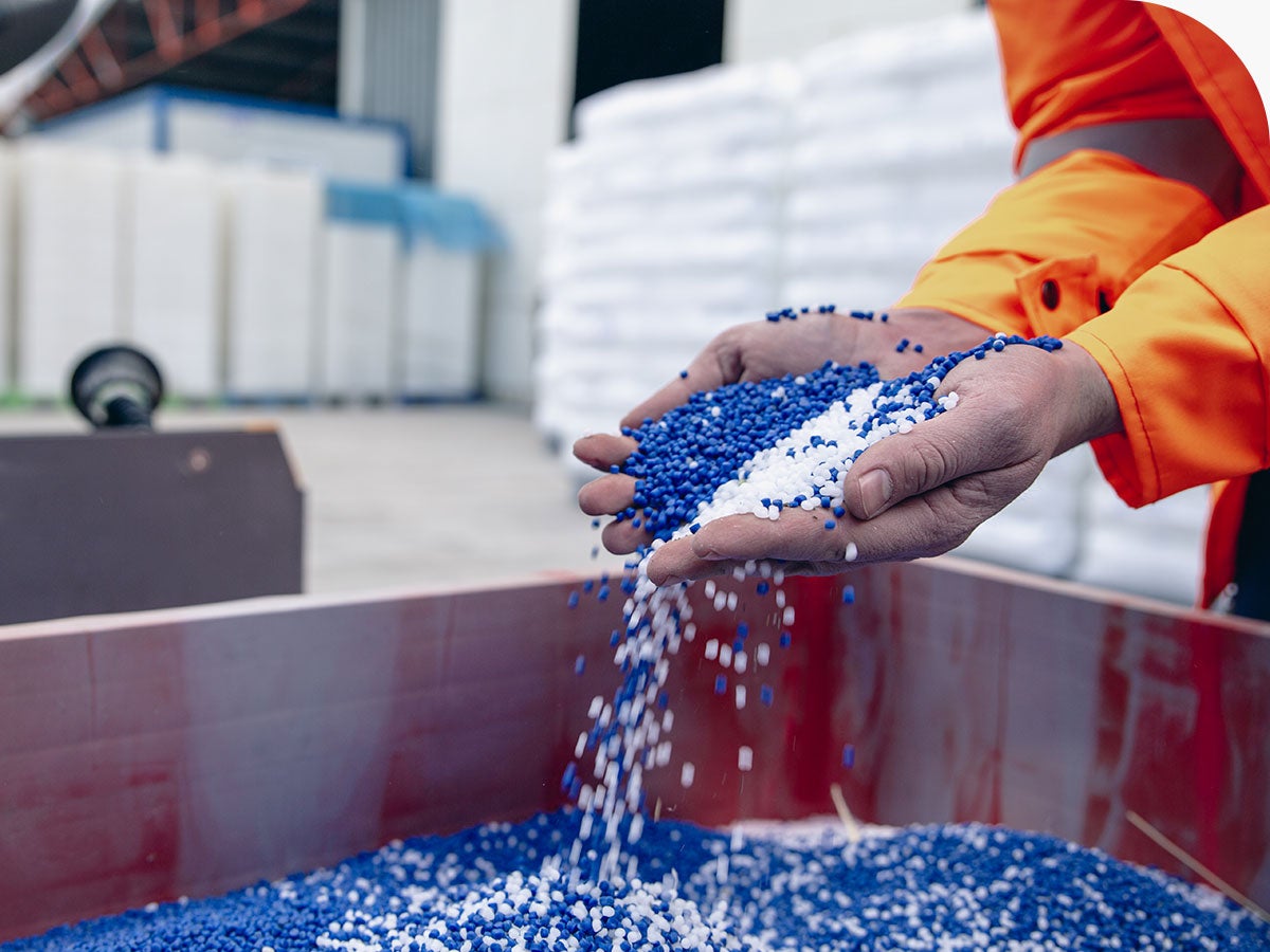 Person in warehouse picking up handfuls of blue and white chemical pellets