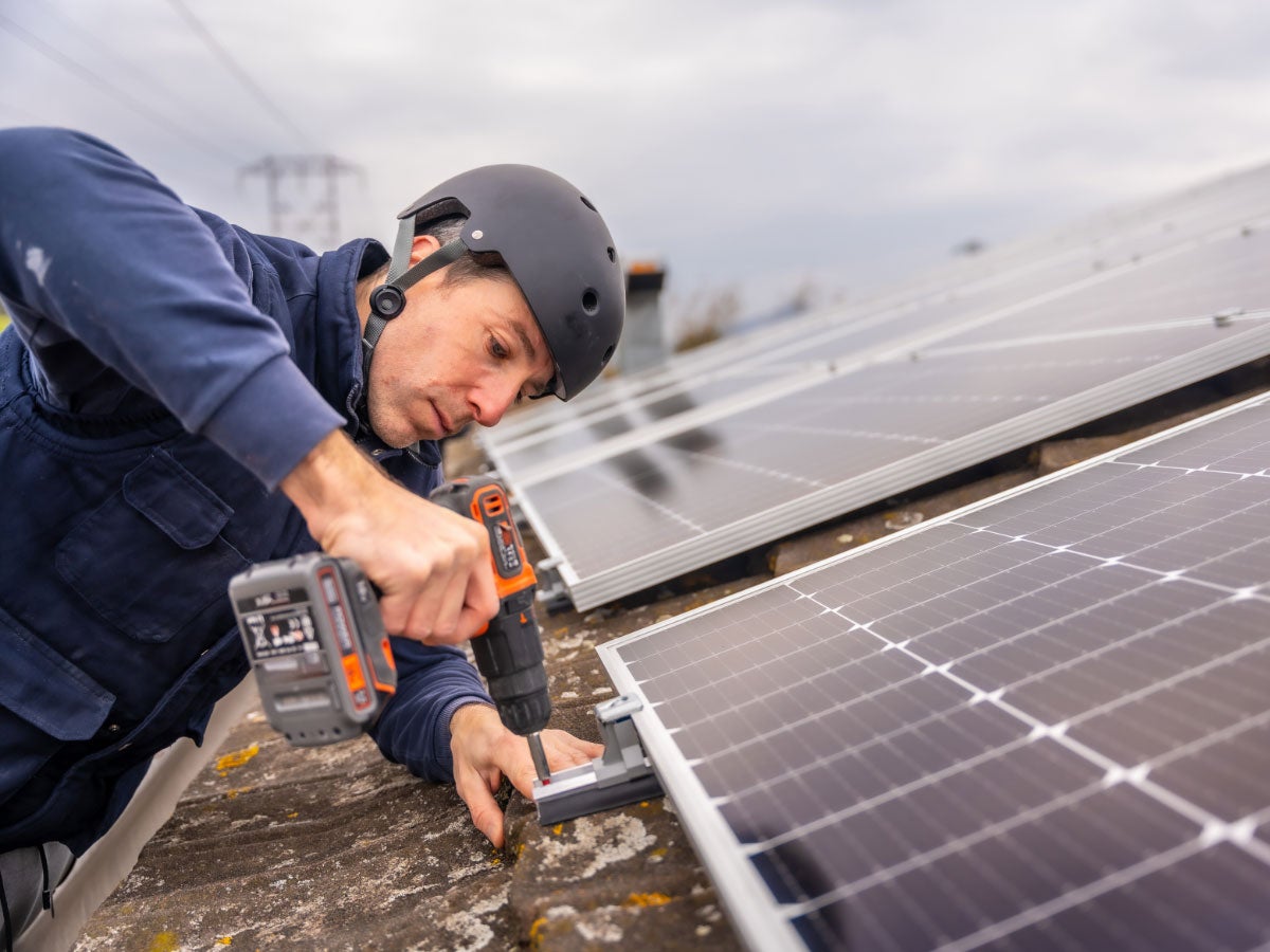 Technician mounting photovoltaic solar modules on the roof of the house.