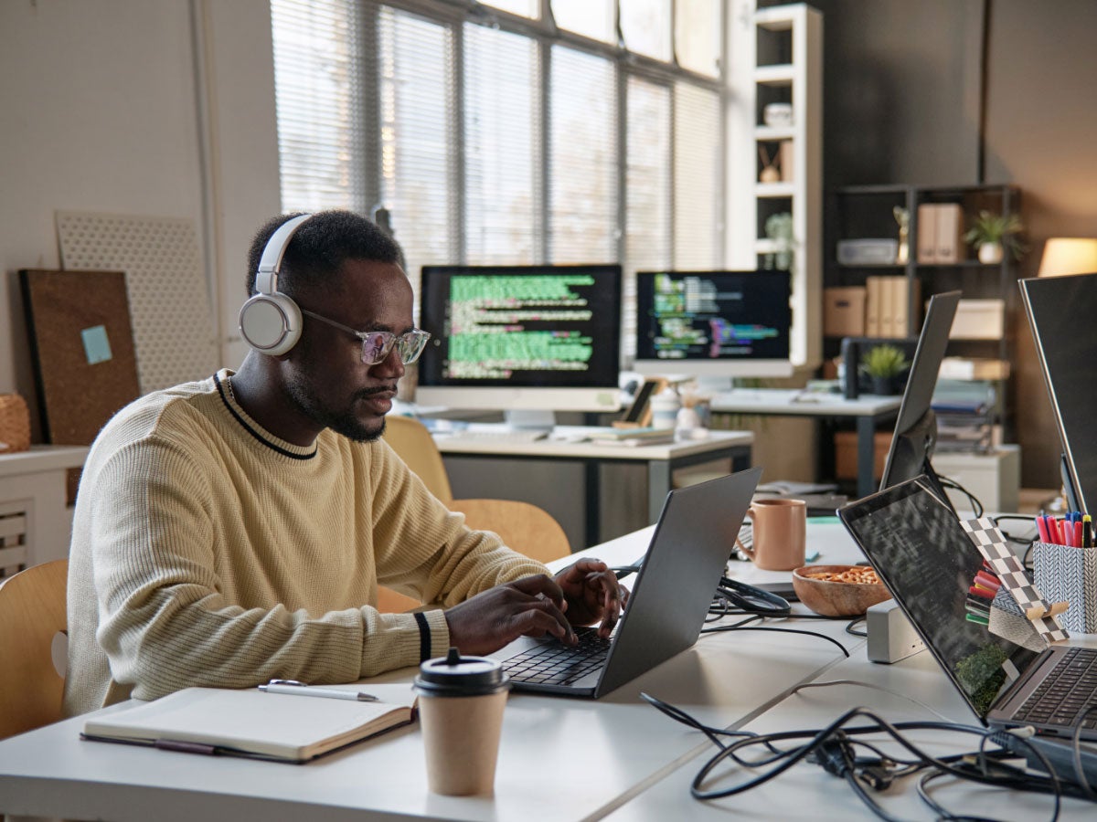 Software developer wearing headphones while coding on a laptop in an office of IT company