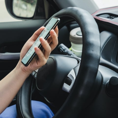 asian woman holding smart phone in drivers seat