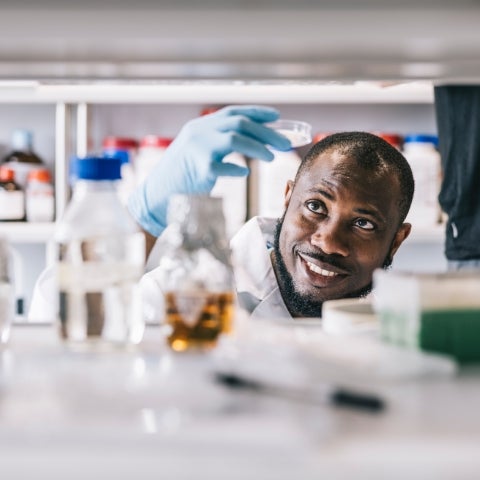 black male scientist looking up at petri dish in hand