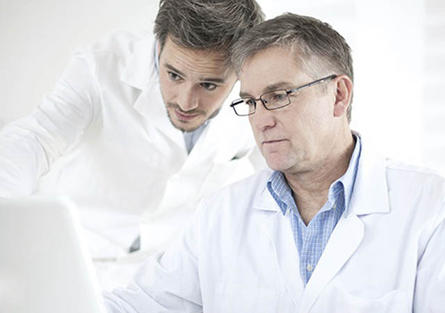 Two men in lab coats looking at a laptop. 