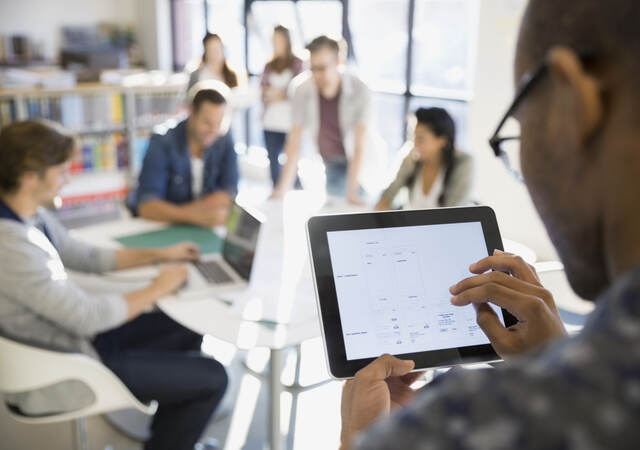 man using and tablet while presenting in front of a room