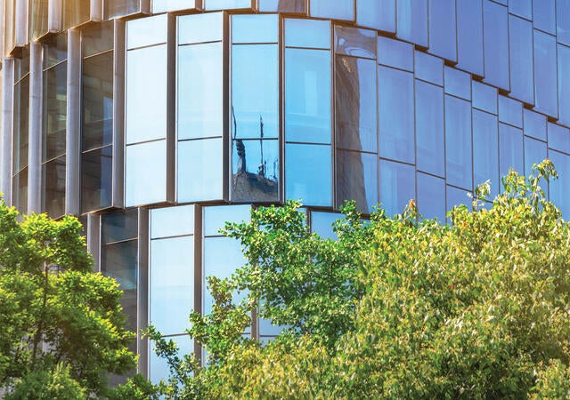 Photo of a blue glass office building with trees in foreground