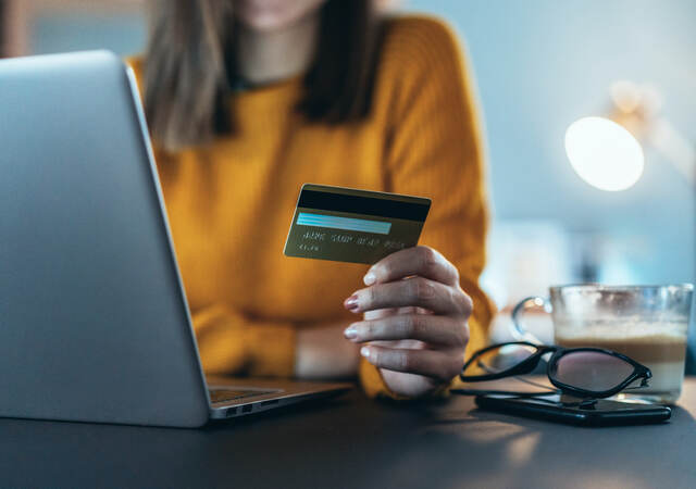 woman holding a credit card and sitting in front of a laptop computer