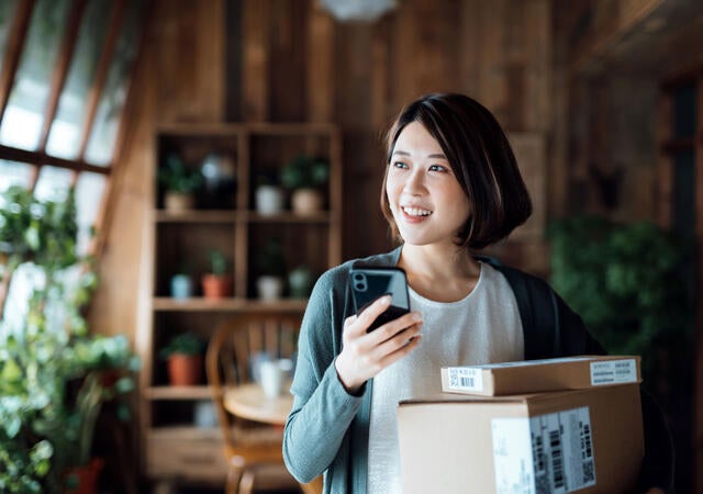 Person holding cellphone and packages in their home