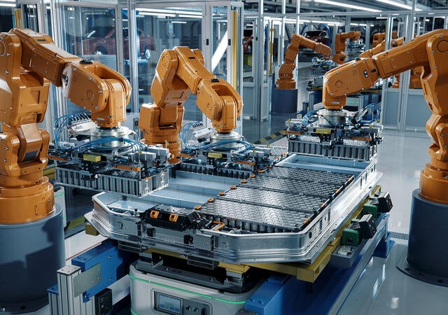 Orange industrial robotic arms assemble EV battery pack on automated production line
