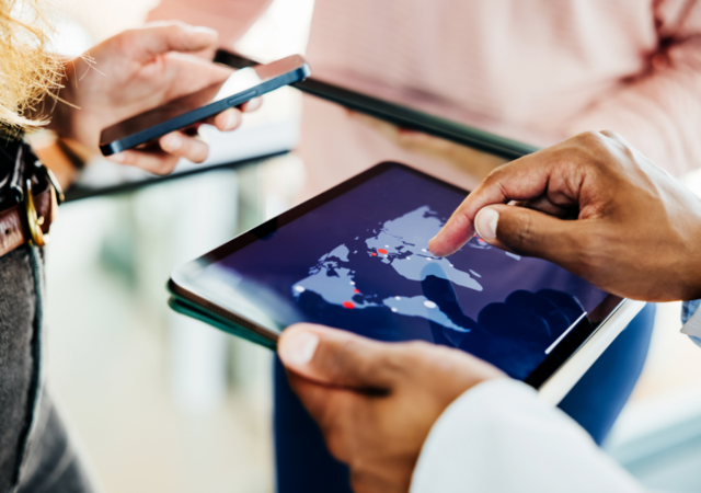 Business professionals collaborate using a digital tablet displaying a global map, indicating international reach and strategic planning