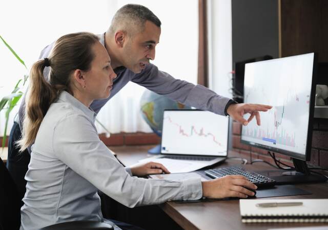 Two people, one is pointing at a chart on a monitor