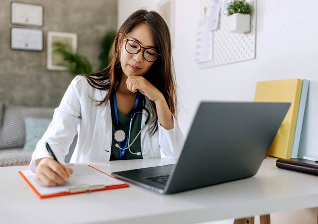 Doctor taking notes while sitting in front of a laptop