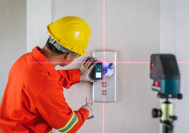 A worker in a hardhat using a laser