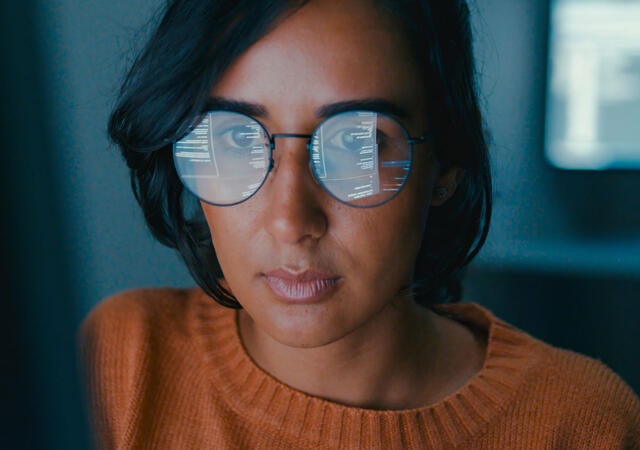 Person working on a computer with the screen reflecting in their glasses