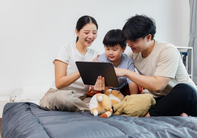 Family spending quality time together on a bed while enjoying an educational activity on a tablet.