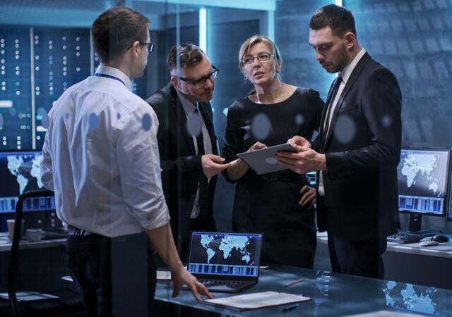 Group of IT colleagues collaborating in front of a tablet and a computer