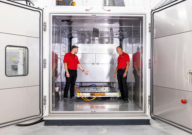 Engineers working inside the performance test chamber with a battery pack placed inside