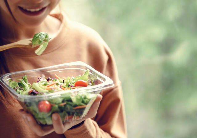 A person eating a salad from a plastic bowl