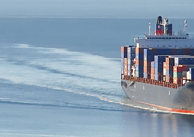 Distant aerial photo of a loaded container ship at sea.