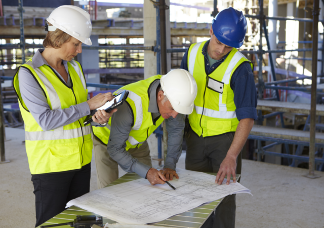 people in safety gear looking at blue prints on construction site