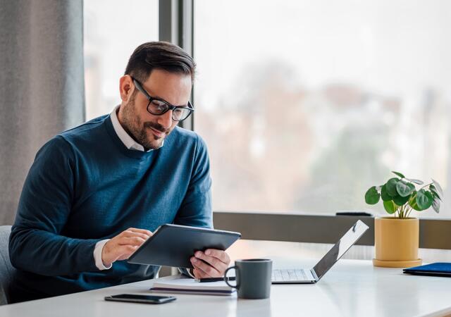 man using tablet at desk by window