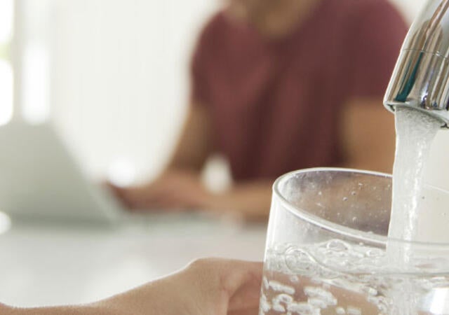 A person filling a water glass at a kitchen sink