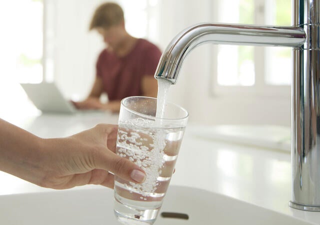 A person filling a water glass at a kitchen sink