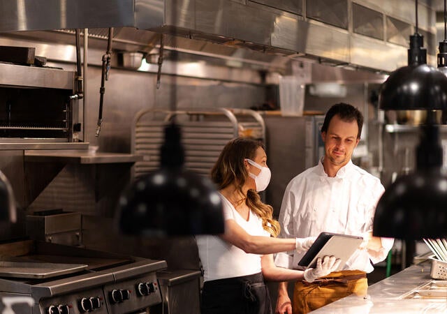 Two people working on a tablet while in a restaurant kitchen